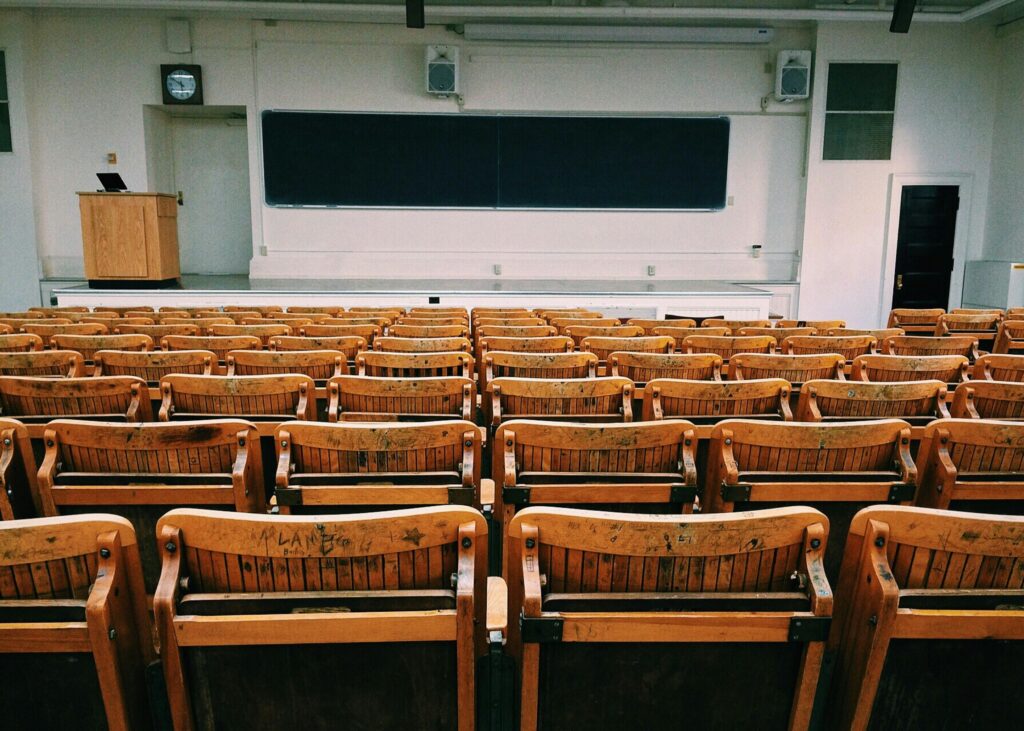 An empty lecture hall featuring wooden chairs and a large blackboard.